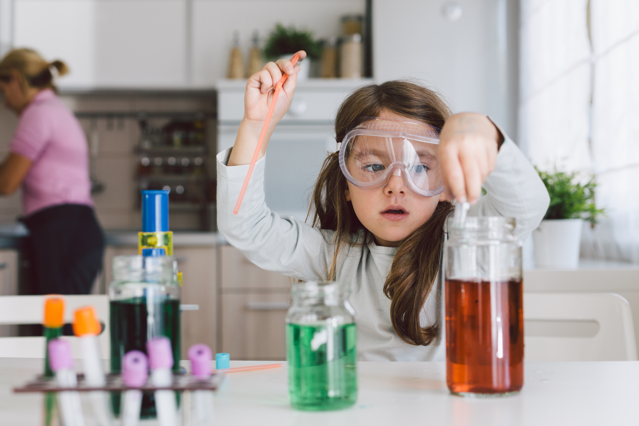 Young child wearing safety goggles, conducting a science experiment in her kitchen at home.