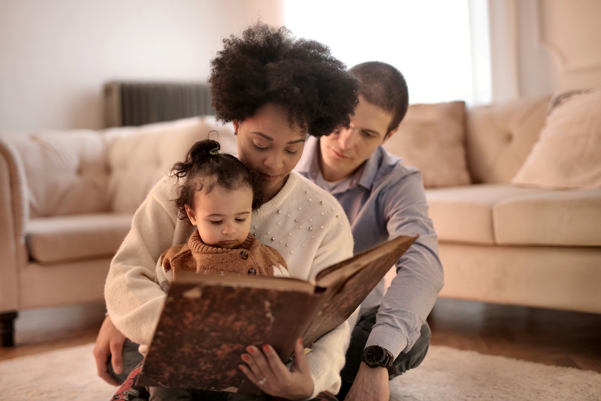 A family sits on the ground together and reads a book.