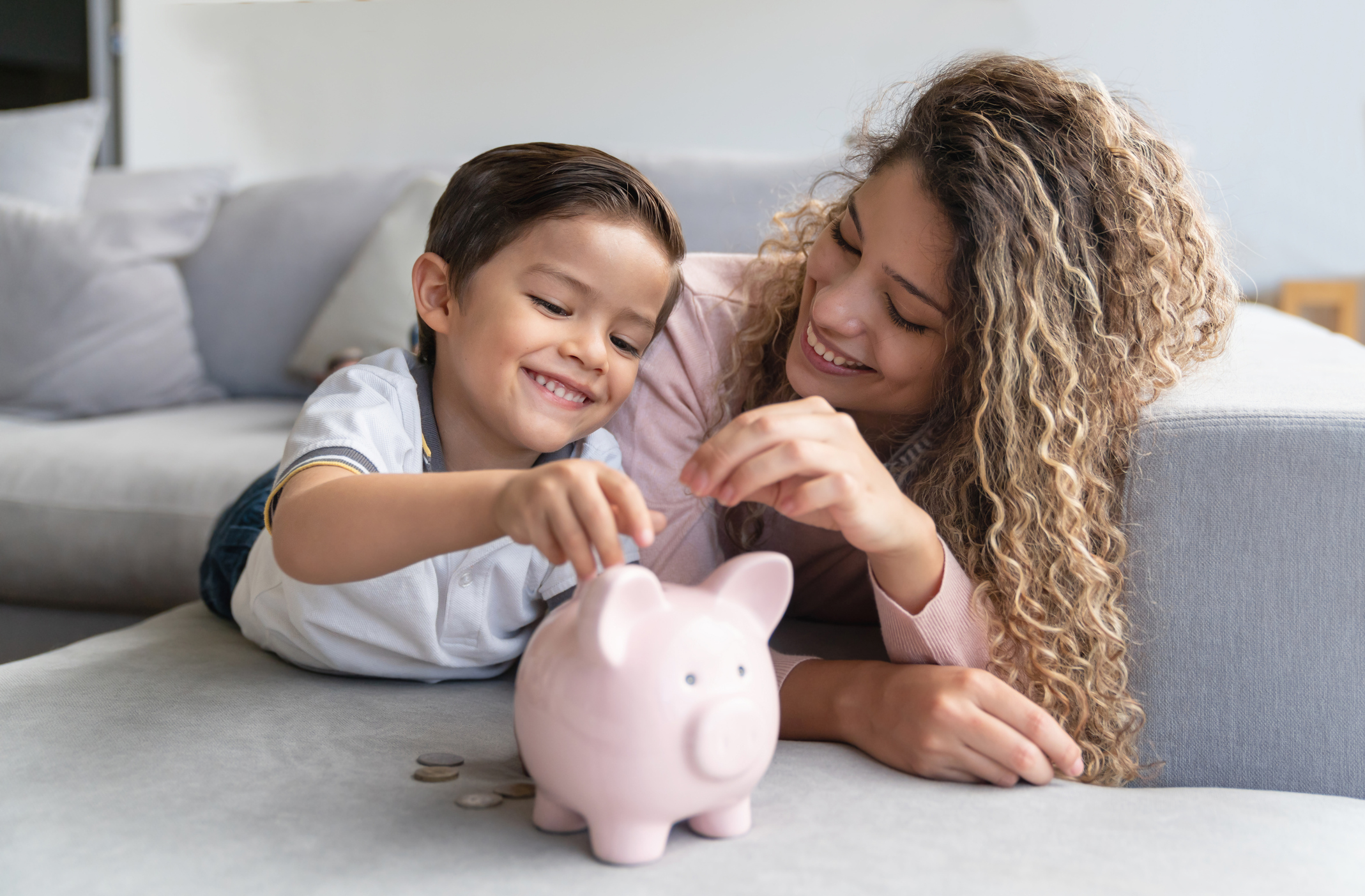 Child putting money in piggy bank with mom.