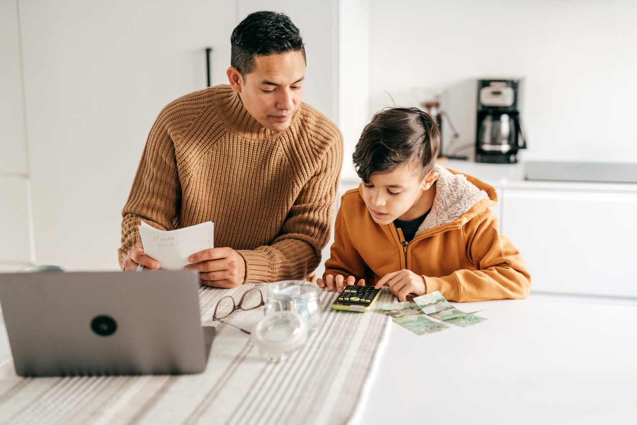 Father and son sitting at a table together, counting cash with a calculator.