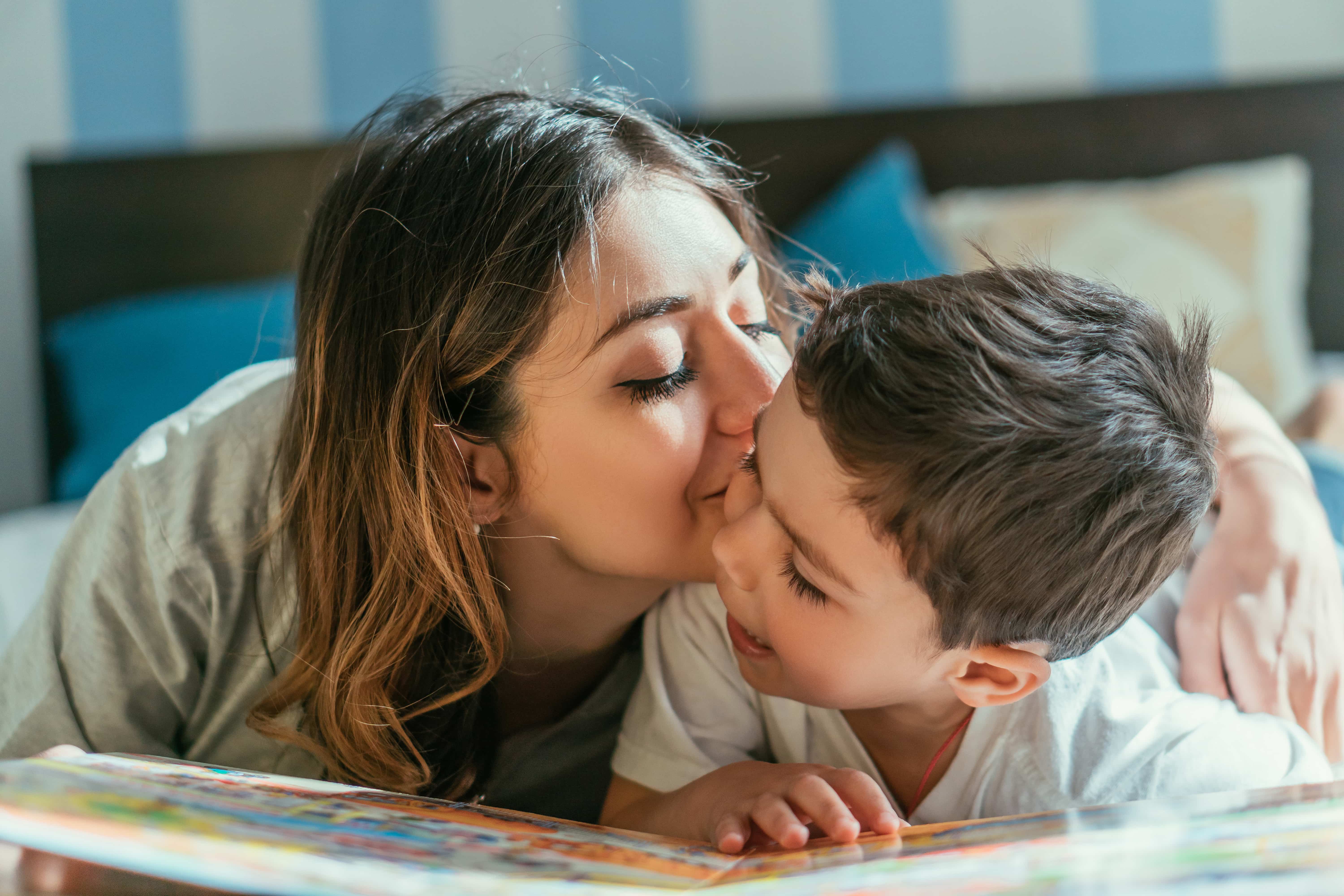 Mom kisses her child as they sit together.