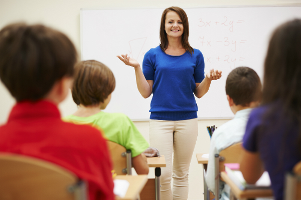 A teacher stands at the front of her class, trying to build excitement by previewing interesting parts of the day