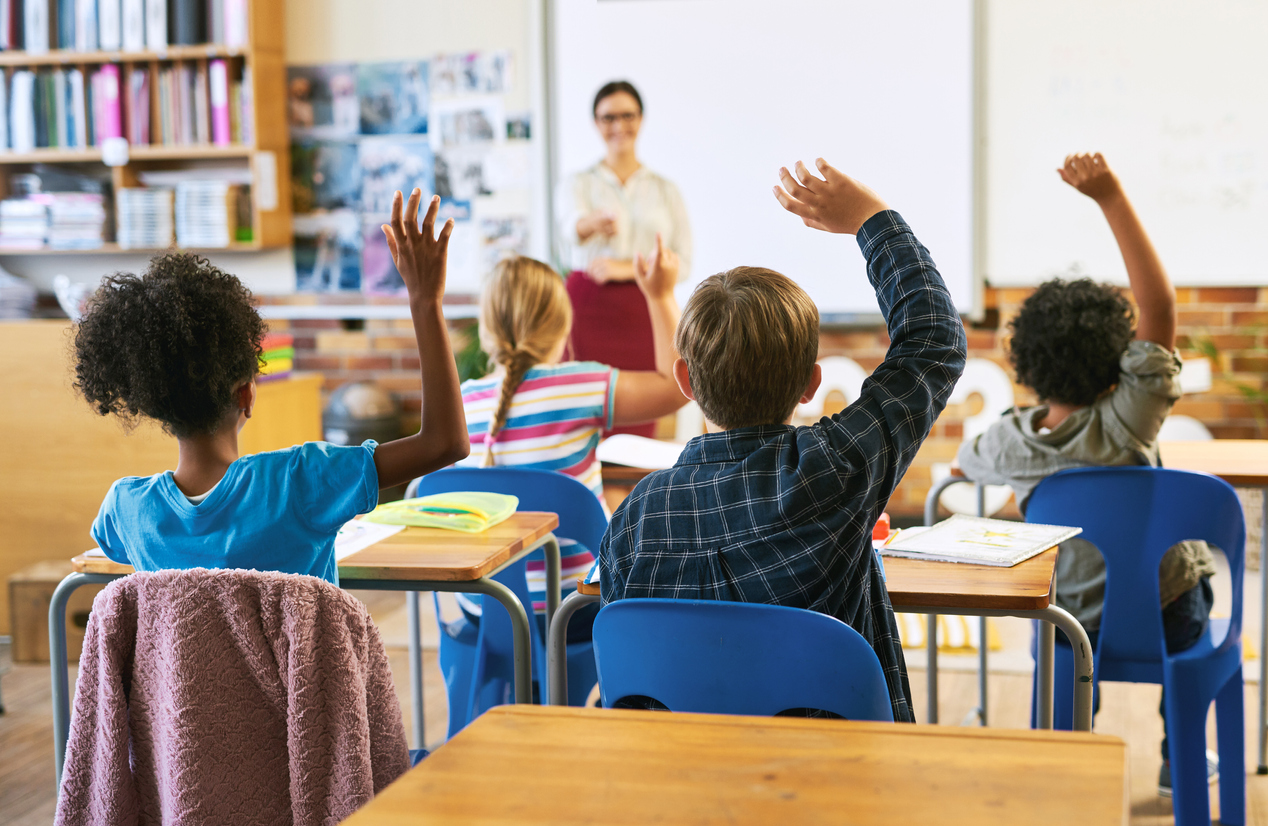 Four middle school students raising their hands to answer their teacher