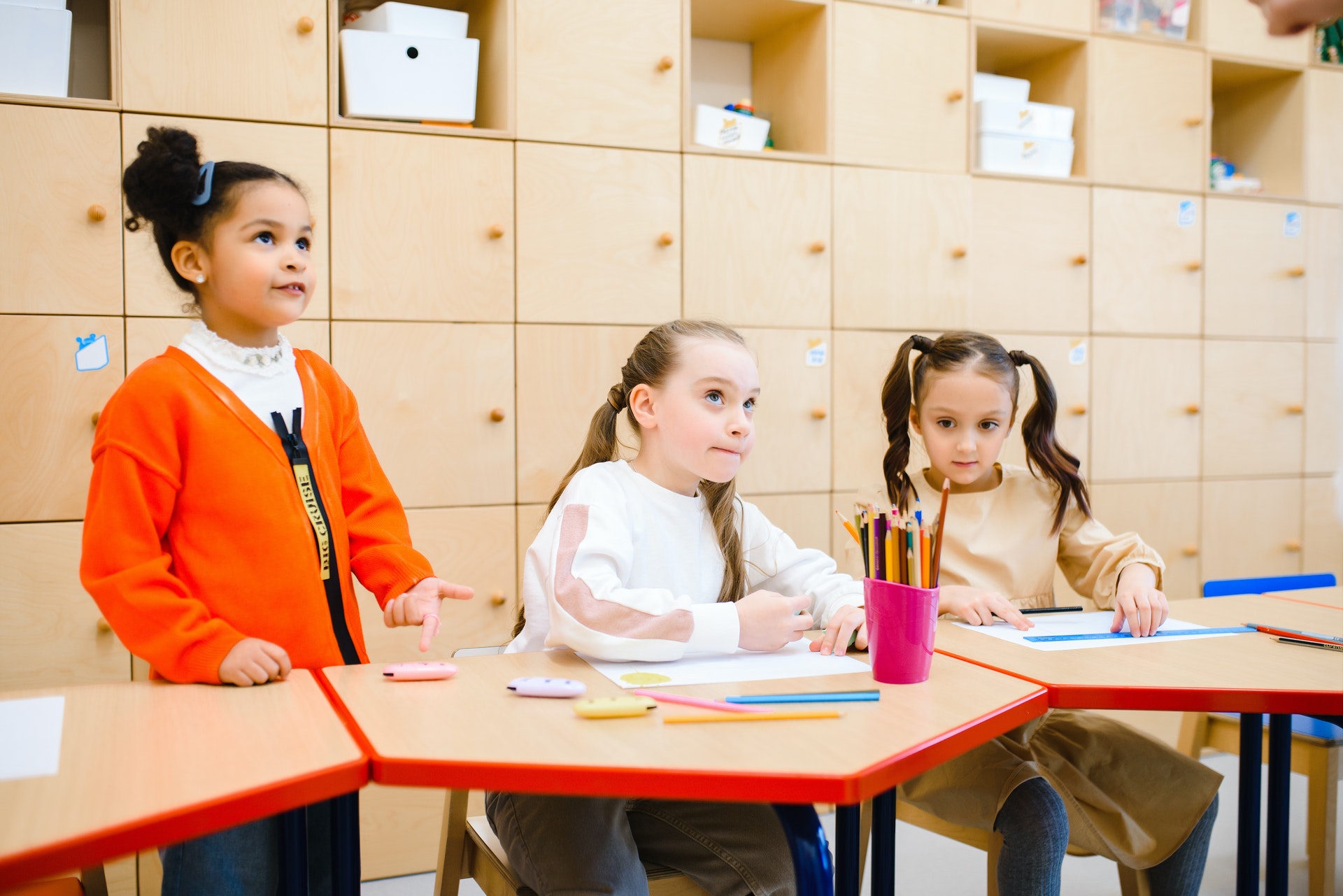 Three students sit a desks and colour in their classroom.