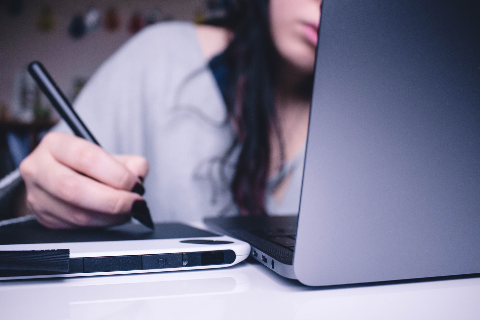 Young woman takes notes on a tablet while using an online learning platform for adults on her computer.