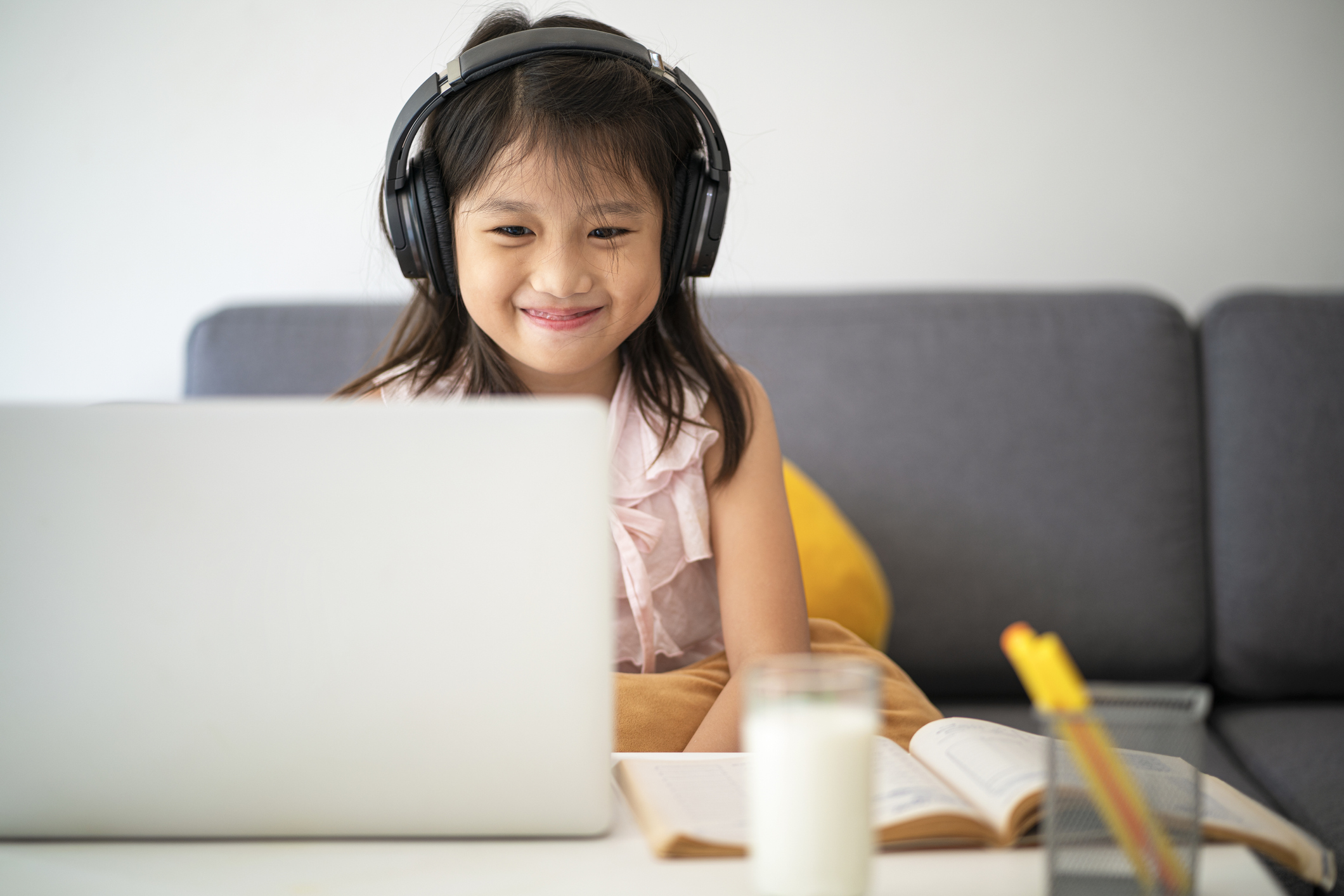 child sitting on couch with headphones on, smiling and learning on a laptop.