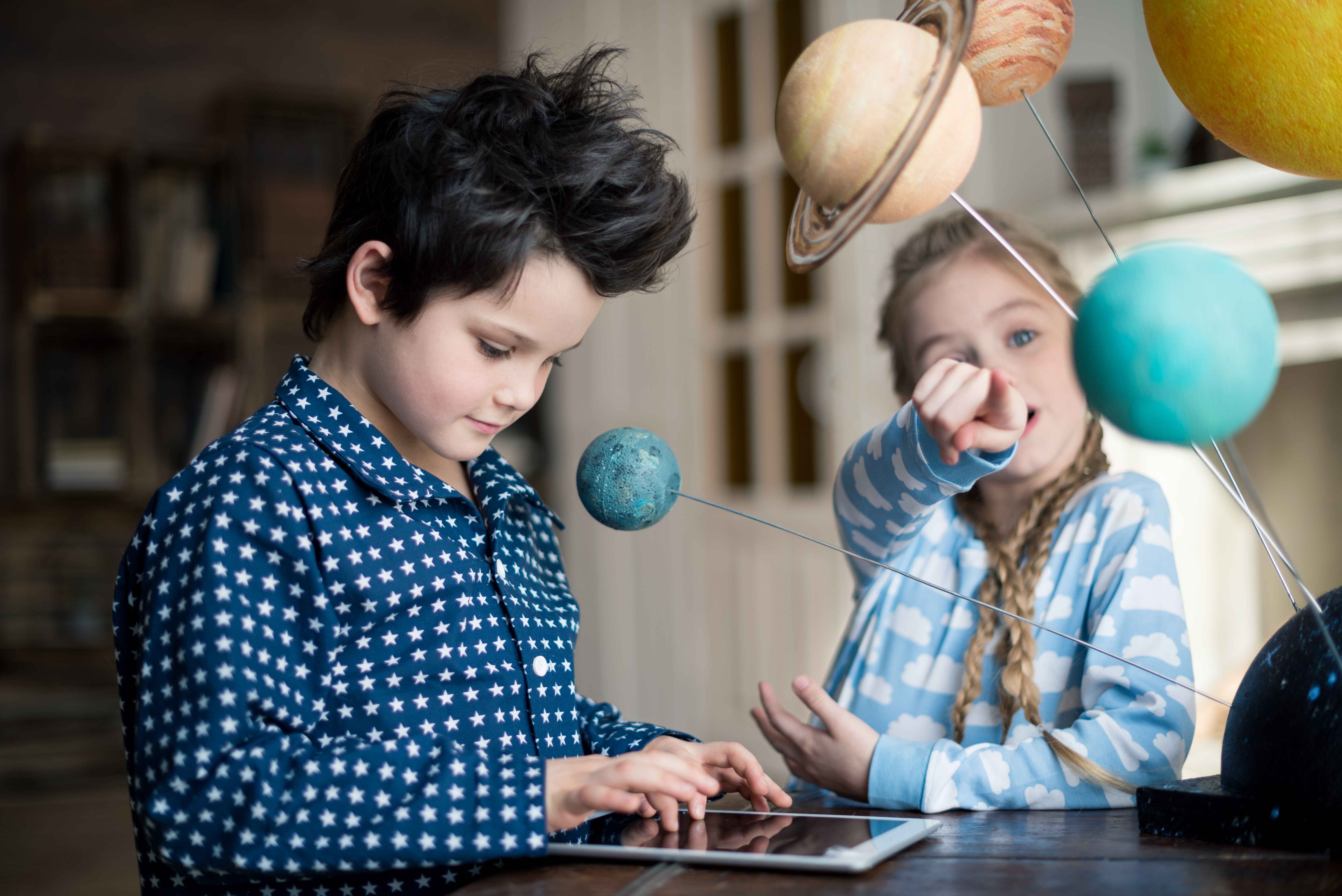 boy using digital tablet while girl pointing on solar system model