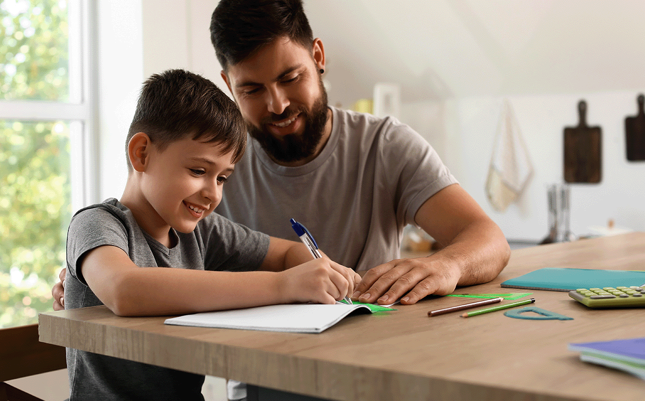 A dad and a son are at a table, both writing, highlighting a bonding moment