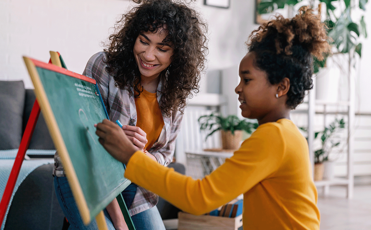 A woman and a girl happily writing together on a blackboard