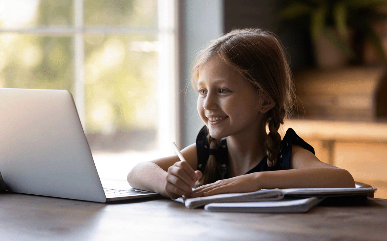 A young girl sits at a table, focused on her laptop