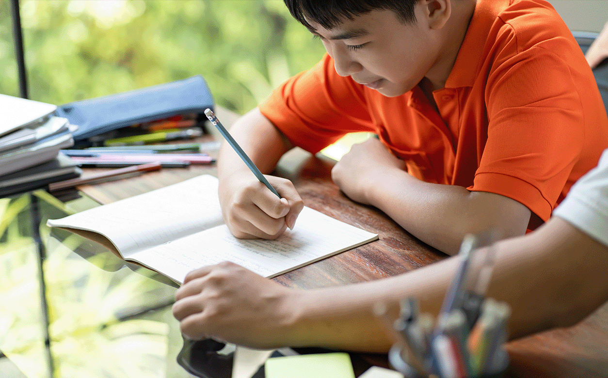 A young boy is focused on writing in a notebook