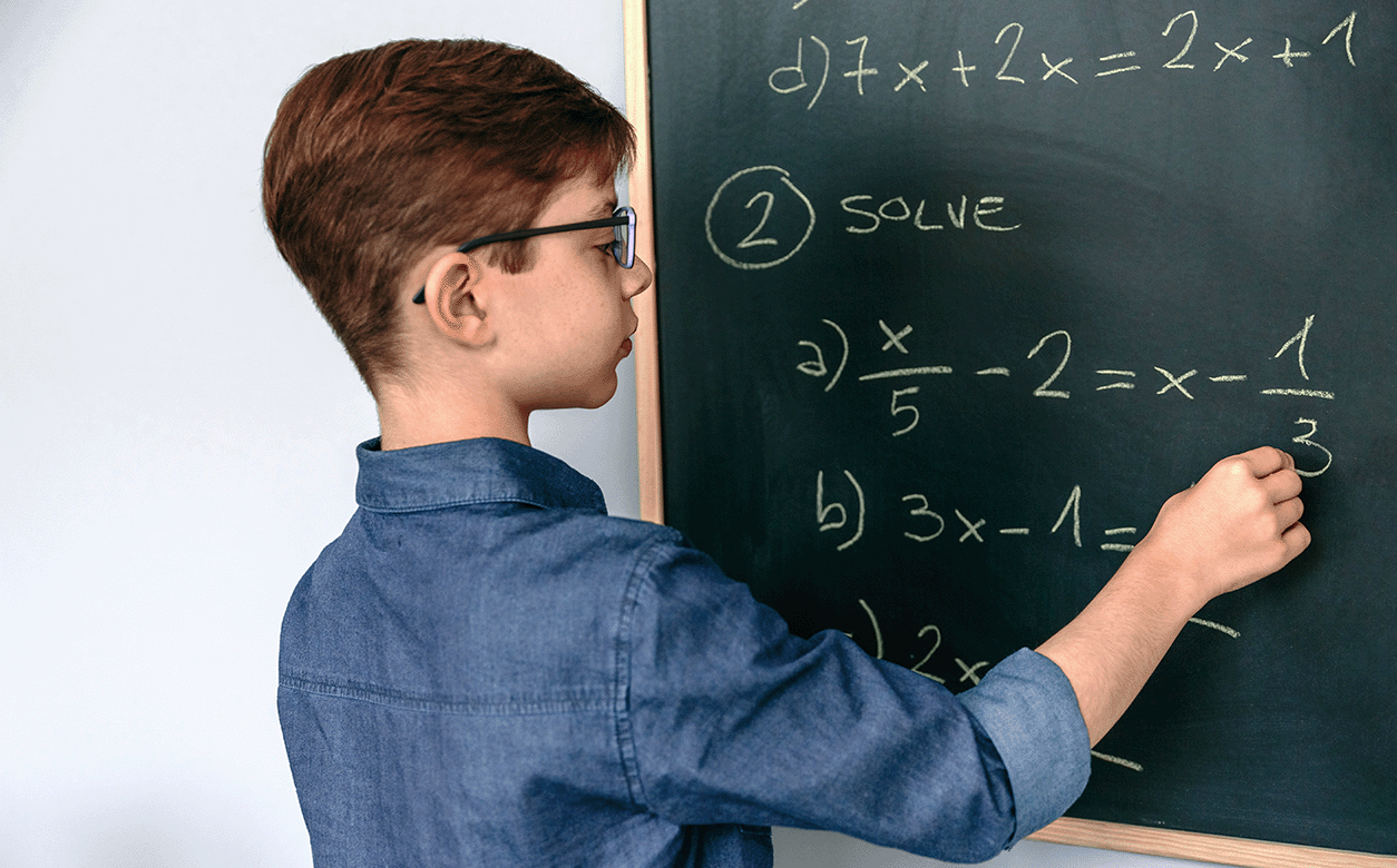 A student is focused on writing math formulas on a blackboard