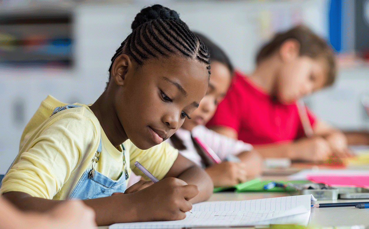 A group of kids focused at their desks and writing
